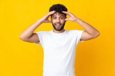 Faslı genç bir adam, sarı arka planda şaşırmış bir ifadeyle izole edilmiş.