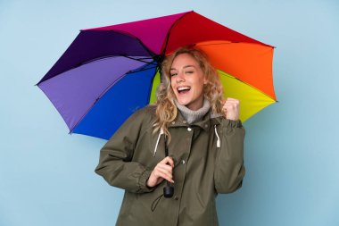 Mavi arka planda bir şemsiye tutan genç sarışın kadın zaferi kutluyor.