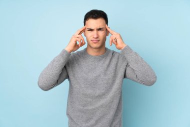 Mavi arka planda izole edilmiş, genç, beyaz, yakışıklı bir adam mutsuz ve hayal kırıklığına uğramış. Olumsuz yüz ifadesi