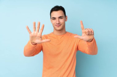 Mavi arka planda izole edilmiş beyaz tenli yakışıklı adam yediyi parmaklarıyla sayıyor.