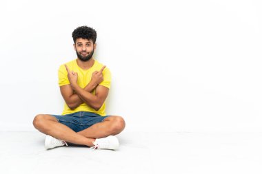 Genç Faslı yakışıklı adam, izole edilmiş arka planda yerde oturuyor. Yan tarafların şüpheleri olduğunu gösteriyor.