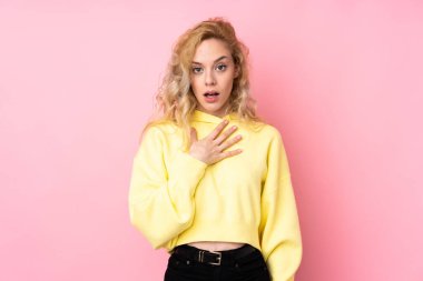 Pembe arka planda izole edilmiş sweatshirt giyen genç sarışın kadın sağa bakarken şaşırmış ve şok olmuştu.