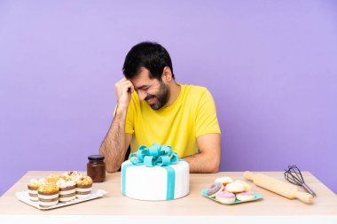 Masadaki adam büyük bir pastayla gülüyor.