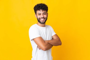 Genç Faslı adam sarı arka planda izole edilmiş, kolları bağlı ve ileriye bakıyor.