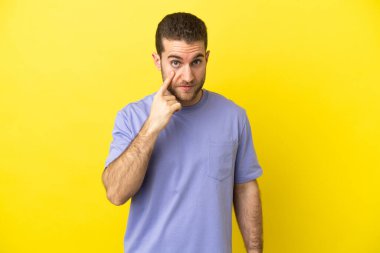 Sarışın yakışıklı adam izole edilmiş sarı arka planda bir şey gösteriyor.