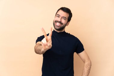 Kafkasyalı yakışıklı adam izole edilmiş arka planda gülümsüyor ve zafer işareti gösteriyor.