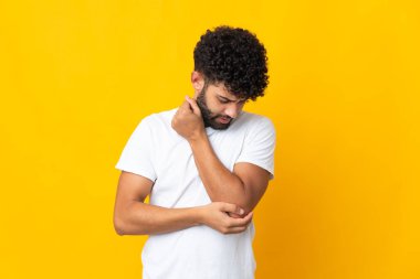 Genç Faslı adam sarı arka planda izole edilmiş, dirsek ağrısı var.