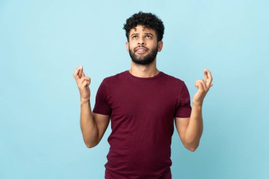 Faslı genç bir adam mavi arka planda izole edilmiş ve şans diliyor.