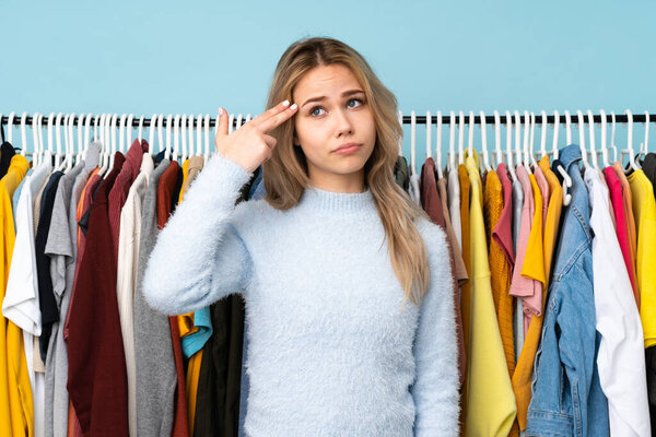 Teenager Russian girl buying some clothes isolated on blue background with problems making suicide gesture