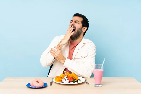 Man Aan Een Tafel Ontbijten Wafels Een Milkshake Geeuwen Bedekken — Stockfoto