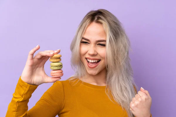 Teenager Girl Isolated Purple Background Holding Colorful French Macarons Celebrating — Stock Fotó