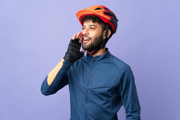 Young Moroccan cyclist man isolated on purple background shouting with mouth wide open to the side