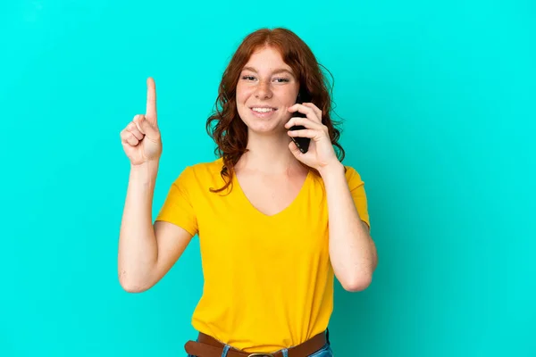 Adolescente Mulher Avermelhada Usando Telefone Celular Isolado Fundo Azul Apontando — Fotografia de Stock