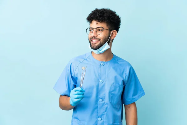 Homem Dentista Marroquino Segurando Ferramentas Isoladas Fundo Azul Olhando Lado — Fotografia de Stock