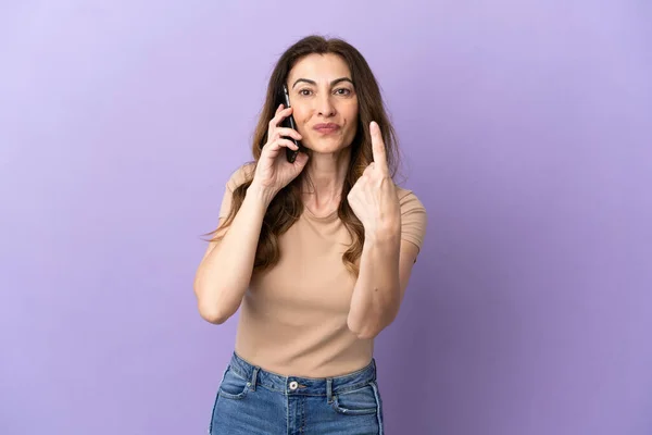 紫の背景に隔離された携帯電話を使用して中年の白人女性がやって来るジェスチャーを行う — ストック写真
