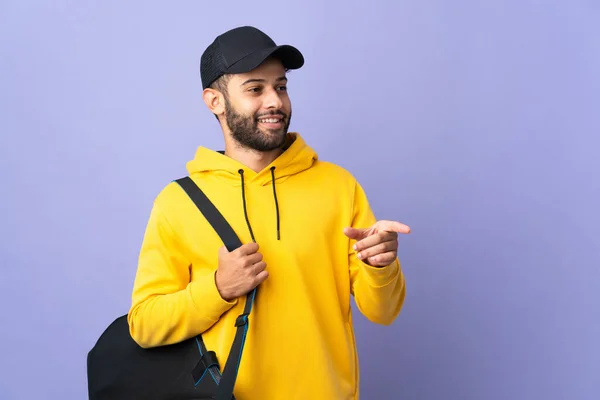 若いですスポーツモロッコ人男性で スポーツバッグは紫色の背景に指をサイドに向けて隔離されています — ストック写真