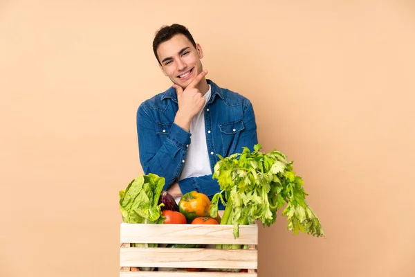 Αγρότης Φρέσκα Λαχανικά Ένα Κουτί Απομονωμένο Μπεζ Φόντο Χαμογελώντας — Φωτογραφία Αρχείου