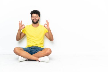 Genç Faslı yakışıklı adam, Zen pozuyla izole edilmiş arka planda yerde oturuyor.