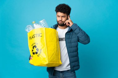 Genç Faslı bir adam, izole edilmiş geçmişi geri dönüştürmek için elinde plastik şişelerle dolu bir çanta tutuyor. Şüpheleri ve düşünceleri var.