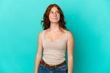 Genç kızılımsı kadın mavi arka planda izole edilmiş şüpheli hareketler yapıyor.