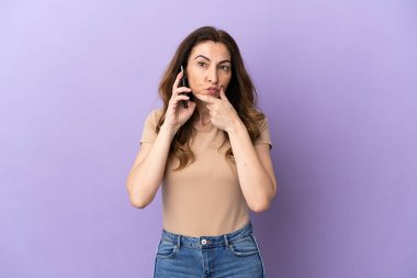 Orta yaşlı beyaz kadın, mor arka planda izole edilmiş cep telefonu kullanıyor.