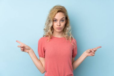 Mavi arka planda izole edilmiş genç sarışın kadın, yan taraftaki kuşkulara işaret ediyor.