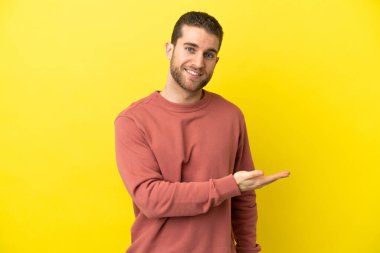 Sarışın yakışıklı adam izole edilmiş sarı arka planda bir fikir sunuyor ve gülümsüyor.