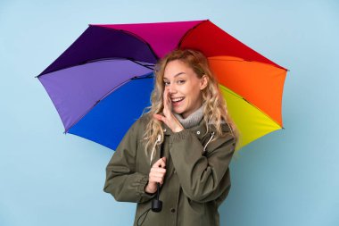 Mavi arka planda bir şemsiye tutan genç sarışın kadın bir şeyler fısıldıyor.