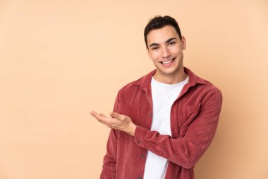 Beyaz tenli yakışıklı adam bej arka planda izole edilmiş bir şekilde bir fikir sunuyor ve gülümsüyor.