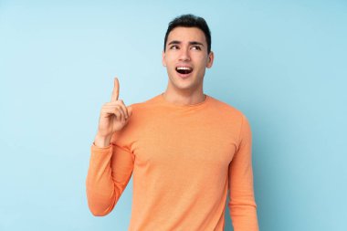 Genç, beyaz, yakışıklı bir adam mavi arka planda izole edilmiş. Çözümü bulmak için parmağını kaldırıyor.