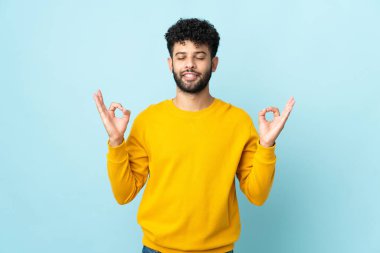 Genç Faslı adam mavi arka planda Zen pozunda izole edilmiş.