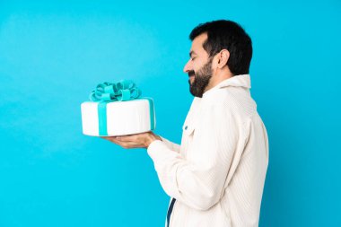 Büyük pastası olan genç ve yakışıklı bir adam izole edilmiş mavi arka planda