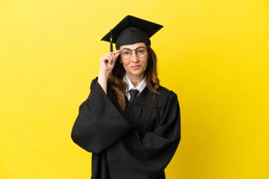 Orta yaşlı üniversite mezunu. Sarı arka planda gözlüklü ve mutlu.