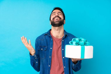 Büyük pastası olan genç yakışıklı bir adam izole edilmiş mavi arka planda gülümsüyor.