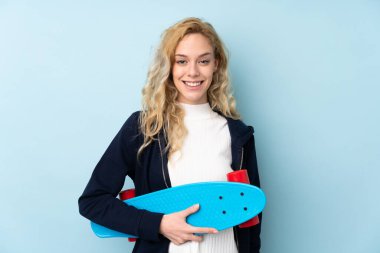 Genç sarışın kadın mavi arka planda tek başına paten kayıyor.