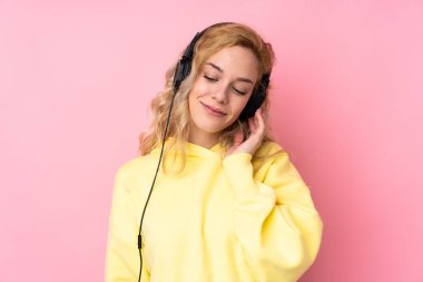 Pembe arka planda izole edilmiş sweatshirt giyen genç sarışın kadın müzik dinliyor.