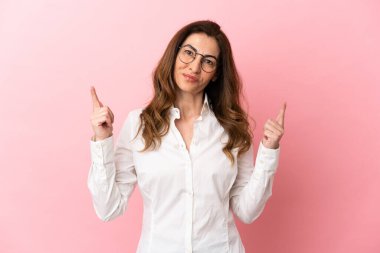 Pembe arka planda izole edilmiş orta yaşlı beyaz kadın harika bir fikre işaret ediyor.