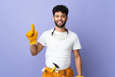 Genç elektrikçi Faslı adam mor arka planda izole edilmiş ve en iyinin işareti olarak parmağını kaldırıyor.