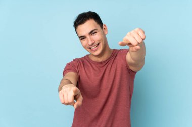 Mavi arka planda izole edilmiş beyaz tenli yakışıklı adam gülümserken seni işaret ediyor.