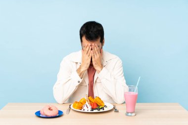 Kahvaltıda waffle yiyen adam ve yorgun ve hasta suratlı bir milkshake.