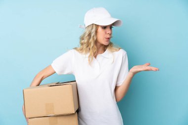 Mavi arka planda izole edilmiş genç bir teslimatçı kadın.