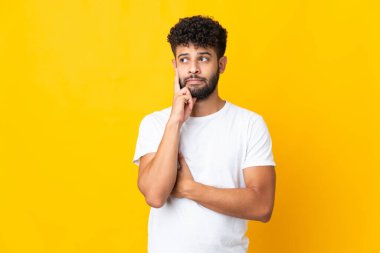 Genç Faslı bir adam sarı arka planda izole edilmiş. Şüpheleri ve düşünceleri var.