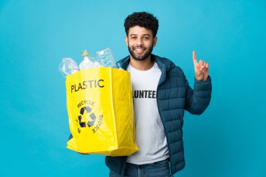 Genç Faslı bir adam, izole edilmiş arka planı geri dönüştürmek için plastik şişelerle dolu bir çanta tutuyor.