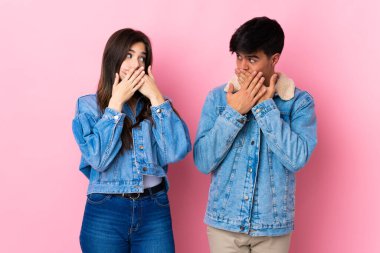 Soyutlanmış pembe arka planda genç bir çift uygunsuz bir şey söyledikleri için ağızlarını ellerle kapatıyor.