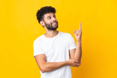 Sarı arka planda izole edilmiş genç Faslı adam harika bir fikre işaret ediyor.