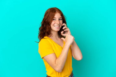 Mavi arka planda izole edilmiş, gururlu ve kendini beğenmiş cep telefonu kullanan genç bir kadın.