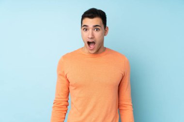 Mavi arka planda yalıtılmış beyaz, yakışıklı, şaşırtıcı bir yüz ifadesi olan genç adam.