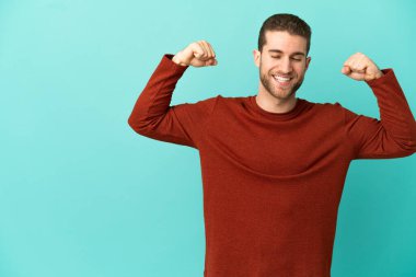 Yakışıklı sarışın, soyutlanmış mavi arka planda güçlü bir jest yapıyor.