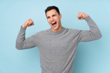 Mavi arka planda izole edilmiş beyaz yakışıklı bir adam zaferi kutluyor.