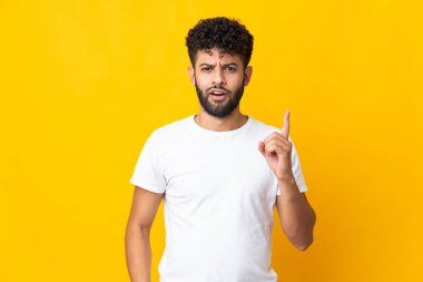 Sarı arka planda izole edilmiş genç Faslı bir adam parmak kaldırarak çözümü bulmaya çalışıyor.
